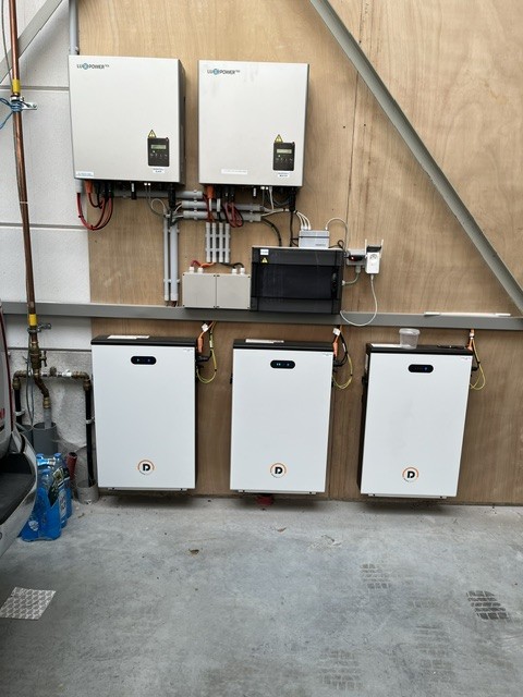 Two inverters above three home batteries against a wooden wall