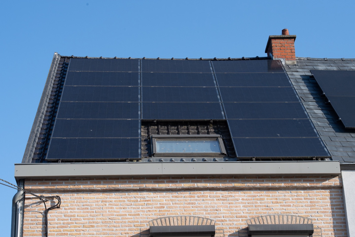 Black solar panels around a roof window on a brick home