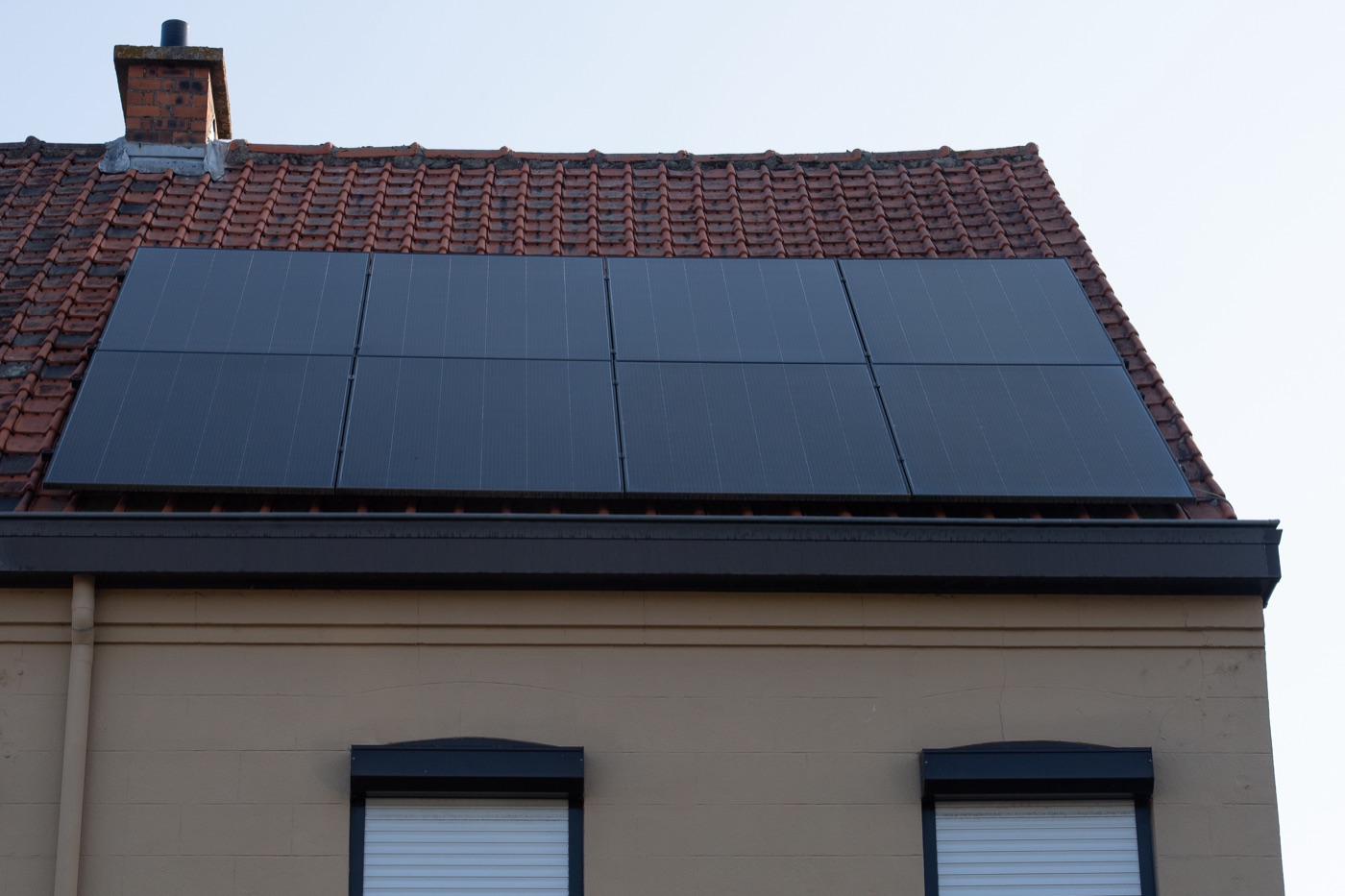 Black solar panels on a red tiled roof above a pale facade