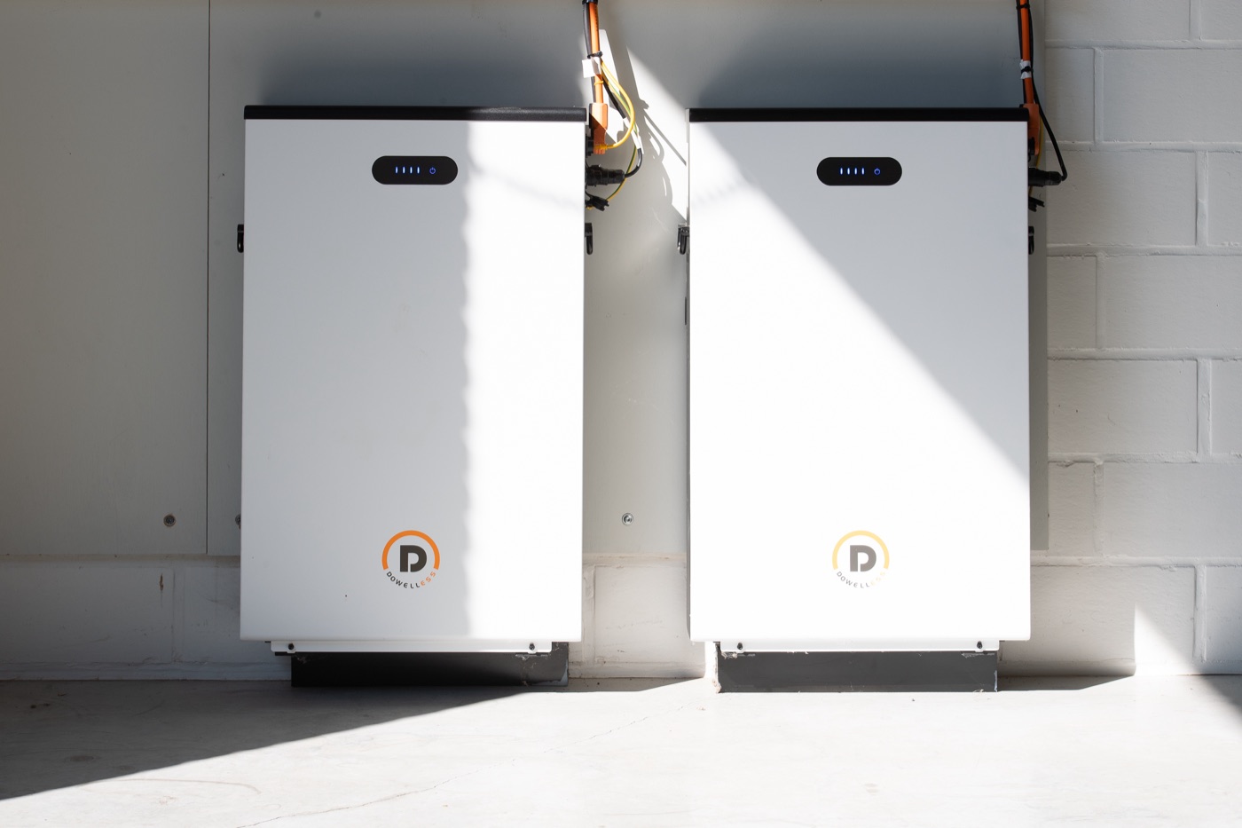 Twee witte thuisbatterijen tegen een witte muur in een technische ruimte