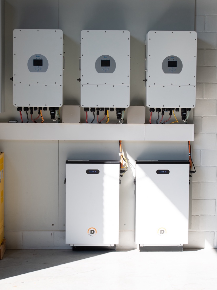 Drie omvormers boven twee thuisbatterijen in een technische ruimte